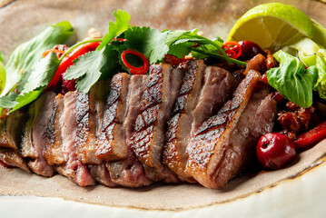 A beautifully plated dish featuring grilled steak, garnished with fresh herbs, colorful peppers, and lime on a large, unique serving platter, set against a dark background.