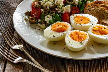 Delicious breakfast - boiled eggs with vegetables and feta cheese served on wooden table
