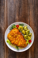 Breaded fried pork chop with fresh vegetable salad and potatoes on wooden table
