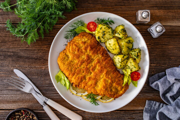 Breaded fried pork chop with fresh vegetable salad and potatoes on wooden table
