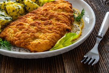 Breaded fried pork chop with fresh vegetable salad and potatoes on wooden table
