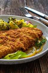 Breaded fried pork chop with fresh vegetable salad and potatoes on wooden table
