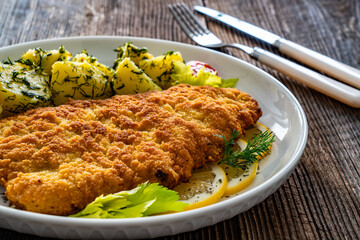 Breaded fried pork chop with fresh vegetable salad and potatoes on wooden table
