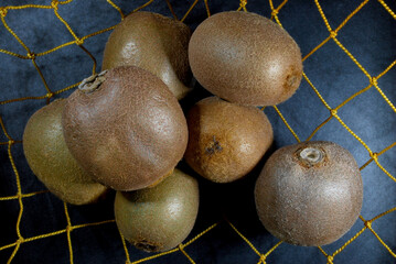 hairy kiwi fruits in a yellow net on a black metal background