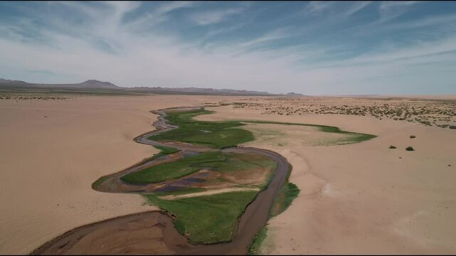 A lonely river flows through the Gobbi Desert, supplying all animals and plants with water. The quadcopter is flying over the only water source in the desert. A river in the sands from the height of a