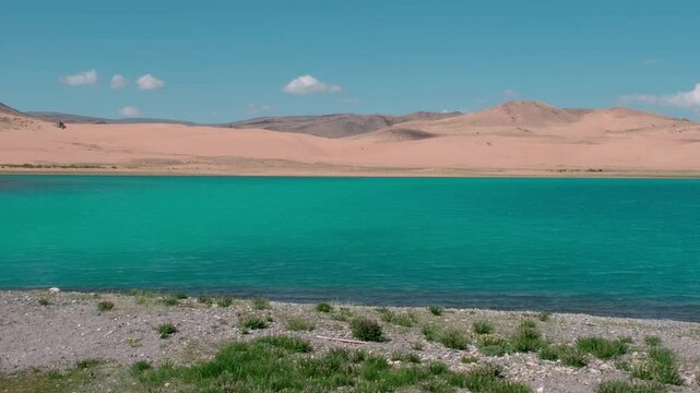 View of a beautiful lake in the Mongolian desert. A lake with a view of the sand dunes. Emerald pond in the hot Gobbi desert. View from the shore to the sand dunes across the lake.