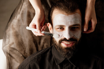 A beautician applies a scrub to the face of an older man in a spa, side light