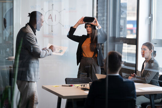 Diverse business professionals in a modern office engaging in a presentation on artificial intelligence. A woman puts on a VR headset, symbolizing innovation. Concept of technology in workplace