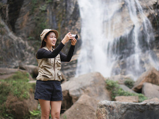 Pretty girl is joyfully posing with her camera in front of a majestic waterfall, embracing the beauty of nature.