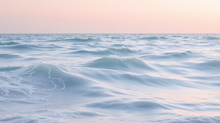 Fototapeta premium Gentle ocean waves roll towards the shore under a soft pink sky, creating a peaceful scene.