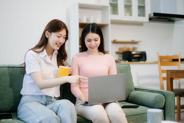 Two women enjoy remote work in a cozy living room, using a laptop while sipping coffee and chatting.