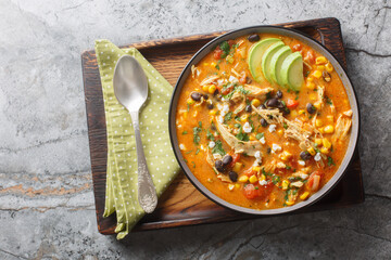 Delicious chicken enchilada soup with corn, tomato, avocado, black beans and cheese closeup on the plate on the table. Horizontal top view from above