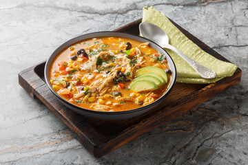 Delicious chicken enchilada soup with corn, tomato, avocado, black beans and cheese closeup on the plate. Horizontal