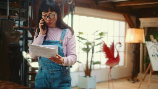 Frustrated  Japanese woman unsatisfied user talking on the phone and holding documents complains about large bills and monthly expenses.