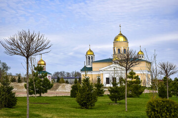 Christian temple, church with green lawn in front of it and gilded domes, crosses against cloudy sky. Religious building. Copy space for text.