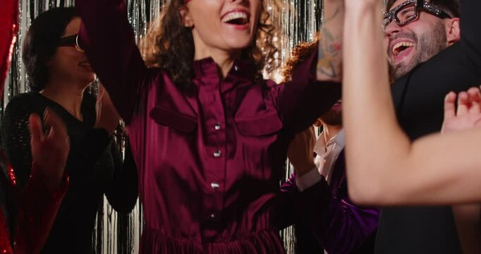 Overjoyed woman in trendy sunglasses enjoying being on party with friends, clapping hands, exclaiming and foolishing around, dancing to music carefree. People, celebration and partying concept 