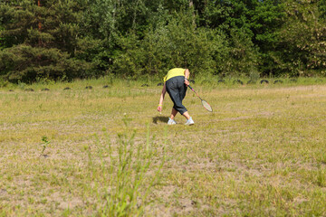 Woman bending down to pick up a shuttlecock while holding a badminton racket