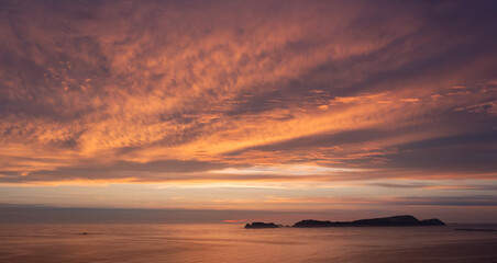 Vibrant sunset illuminating clouds over calm ocean and islands