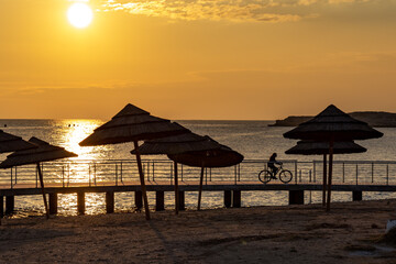 A cyclist on a bike rides along a pier on the beach of sea in tourist resort.at sunset. Backlight.  Mediterranean, Cyprus