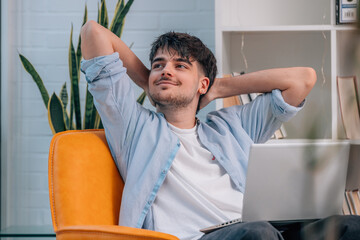 young man or student sitting indoor with laptop and relaxed expression or gesture