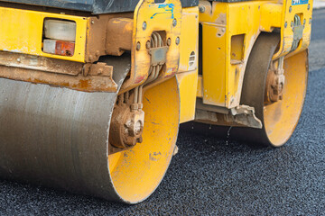 Road construction site with a roller compactor leveling fresh asphalt. Close-up on the machinery,...