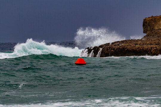 Winter storm in Cyprus. Red buoy and wave crashing on rocks with dark sky. January
