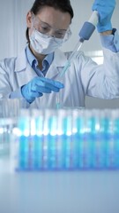 Woman scientist wearing lab coat, blue medical gloves, mask and protective glasses is using...