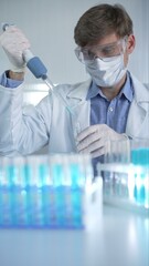 Male scientist researcher, wearing lab coat, white medical gloves, mask and protective glasses is...