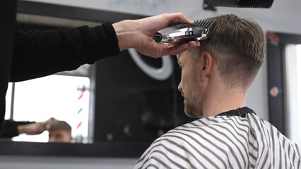 Professional barber trimming male client's hair using electric razor, creating precise haircut in contemporary barbershop setting with sleek styling tools