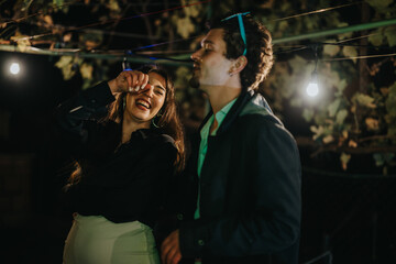 An image depicting a happy atmosphere with two friends laughing and engaging in a celebration, illuminated by string lights. Perfect for concepts depicting friendship, nightlife, and convivial moments