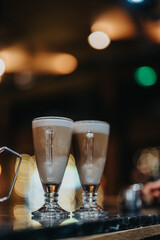 Two latte glasses displayed on a polished surface, illuminated by warm ambient bokeh lighting, conveying a cozy and inviting atmosphere.