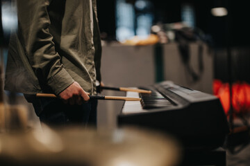 A focused depiction of a performer resting with drumsticks on a digital piano during band practice.