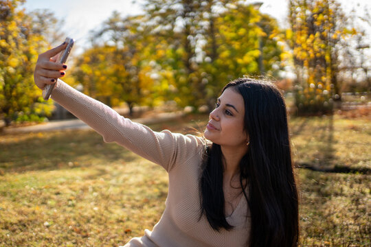 Young woman taking a selfie in a sunny autumn park