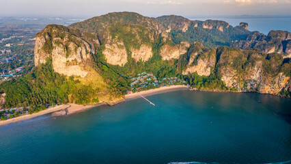 Aerial view of tropical limestone cliffs and turquoise sea in Krabi, Thailand, showing pristine beaches and dramatic coastal rock formations under sunny weather