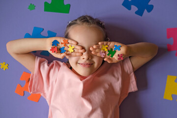 The child holds colored puzzle pieces in his hands, closing his eyes. The generally accepted international symbol of autism