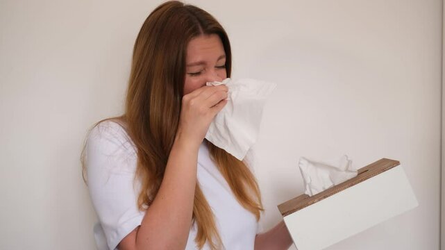young woman suffering from allergies blowing her nose into a paper napkin