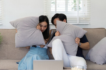 Obraz premium Couple hiding behind pillows while watching a scary movie at home