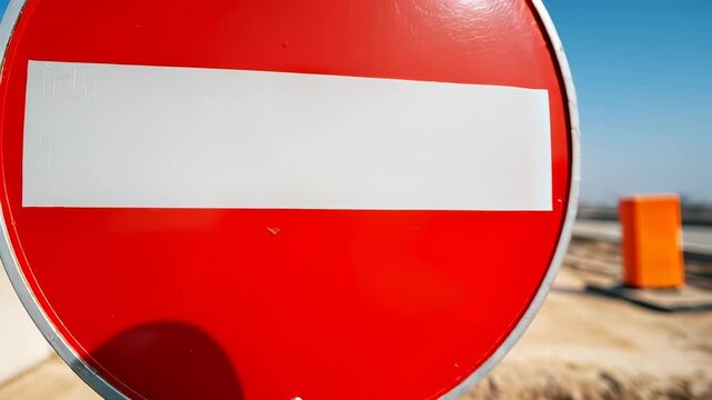Red no entry road sign near construction site and highway under clear blue sky.