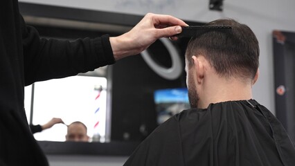 Fototapeta premium Professional hairdresser styling male client's hair, mirror reflecting classic barber pole, salon interior with modern grooming ambiance