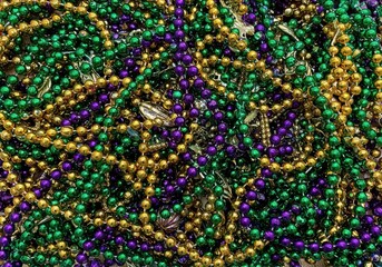 A close-up photograph captures a dense tangle of Mardi Gras beads, showcasing a variety of colors and textures.