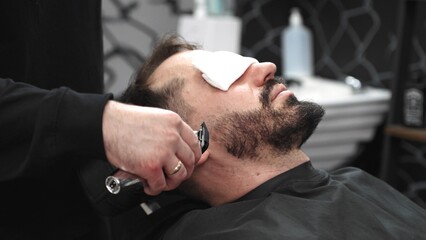 Professional barber grooming client's beard using electric razor, delivering precise trimming in contemporary barbershop setting