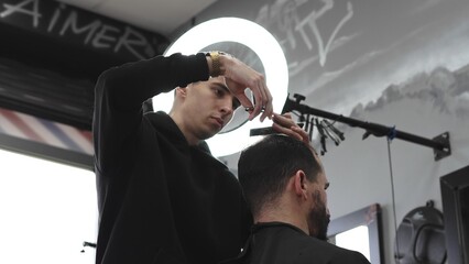 Skilled barber trimming client's hair using professional scissors, creating precise hairstyle in contemporary salon with modern interior and relaxed atmosphere