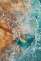 Fototapeta premium Aerial view of ocean waves crashing on sandy shore, showcasing vibrant turquoise water and rock formations, perfect for travel and nature themes.