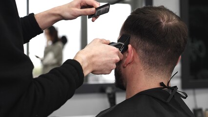 Skilled barber trimming client's hair using electric razor, creating contemporary hairstyle in modern barbershop setting with precise, professional technique