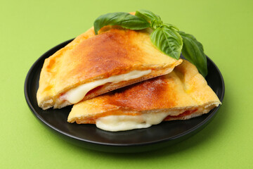 Pieces of delicious calzone pizza with mozzarella, tomatoes and basil on green background, closeup