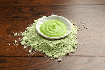 Pile of dry wasabi powder and bowl with paste on wooden table, closeup