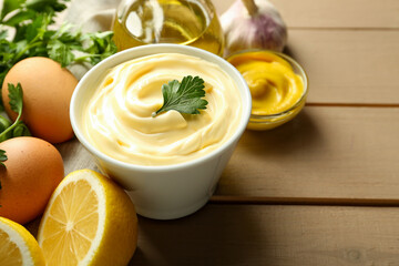 Delicious mayonnaise sauce in bowl and ingredients on wooden table, closeup. Space for text