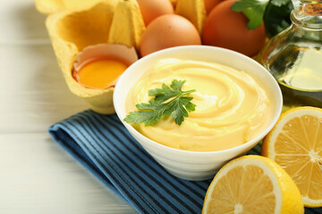 Delicious mayonnaise sauce with parsley in bowl and ingredients on white wooden table, closeup