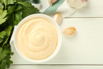 Delicious mayonnaise sauce in bowl, garlic and parsley on white wooden table, flat lay. Space for...
