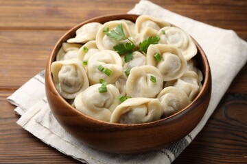 Delicious dumplings with fresh green onion and parsley on wooden table, closeup